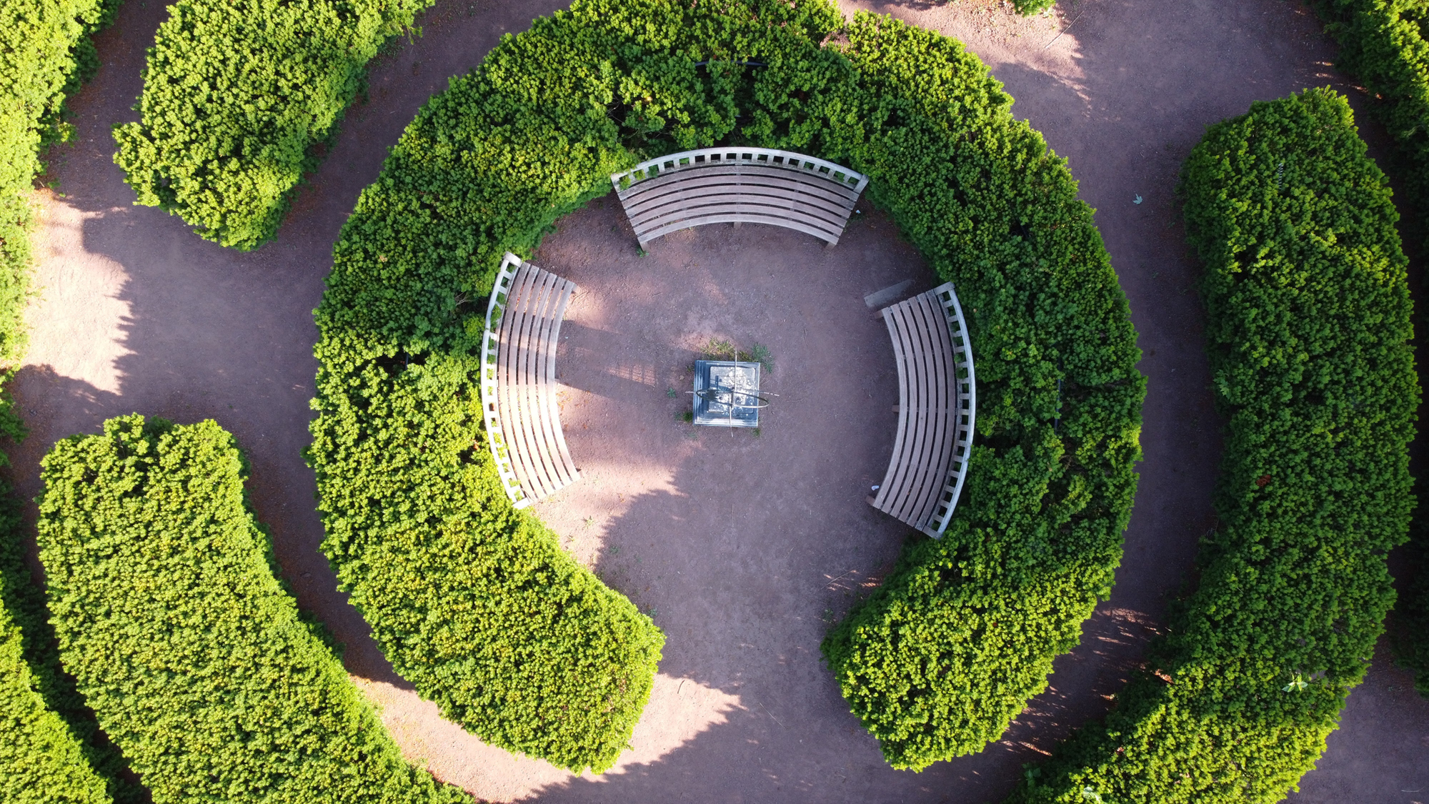 An aerial view of concentric bushes that are divided surrounding a group of three benches